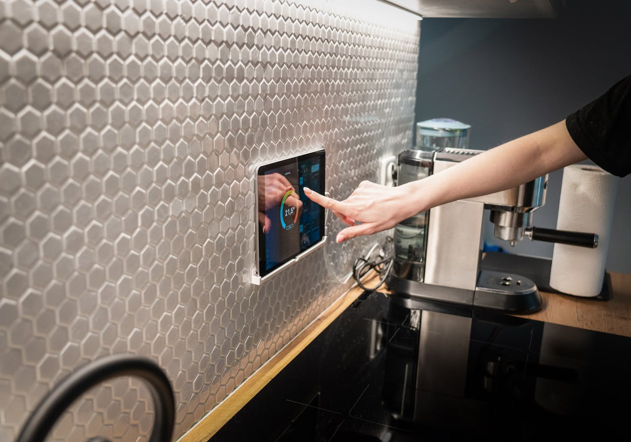 A modern kitchen with a touchscreen smart home control panel integrated into a hexagon-patterned wall.