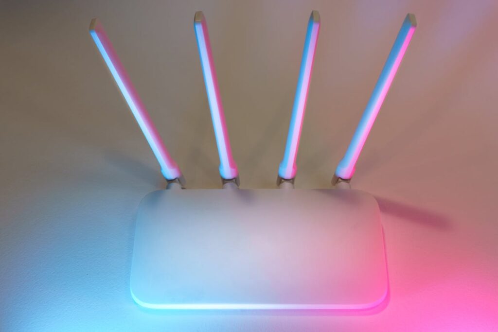 pexels photo 29711663 Sleek white wireless router with four antennas emitting soft blue and pink light.